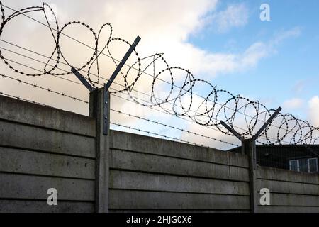 silhouette di filo di rasoio di sicurezza e filo spinato sulla parte superiore di un pannello parete blu cielo e nuvole Foto Stock