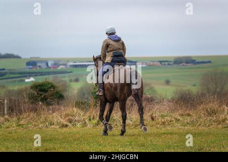 lady equitazione in campagna aperta sotto un cielo blu grigio nuvola d'inverno Foto Stock