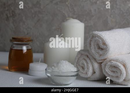 Spa relax massaggio casa cura per il corpo di soia. Candele bianche asciugamani olio in un vaso bottiglia scrub su uno sfondo bianco grigio con spazio per il testo. Salone di bellezza Foto Stock