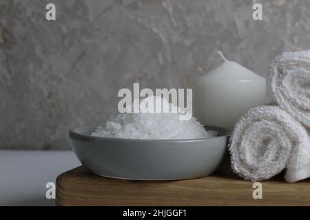 sale per la cura del corpo domestico di scrub del bagno. Il sale grossolano si trova in una ciotola grigia con un cucchiaio di legno asciugamano candela su uno sfondo grigio. Spa relax. Foto Stock