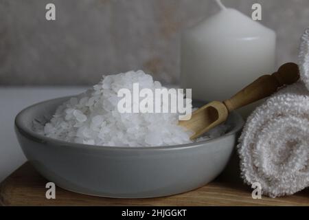 sale per la cura del corpo domestico di scrub del bagno. Il sale grossolano si trova in una ciotola grigia con un cucchiaio di legno asciugamano candela su uno sfondo grigio. Spa relax. Foto Stock