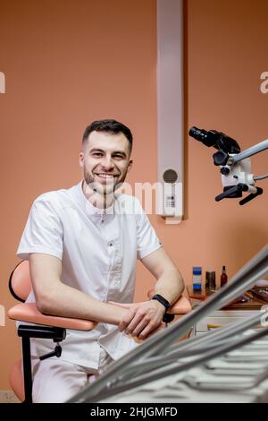 Un dentista maschile guarda al microscopio. Odontoiatria moderna che utilizza nuove tecnologie. Foto Stock