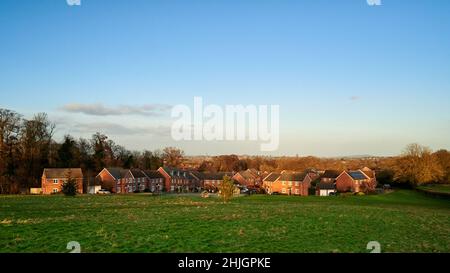 ampio scatto di case suburbane sotto il cielo blu con parco di erba in primo piano sotto il sole invernale Foto Stock