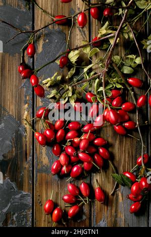 Frutti di bosco di rose con ramificazione e foglie su vecchio sfondo di legno scuro. Riserve autunnali di vitamine per l'inverno. Disposizione piatta, spazio di copia Foto Stock