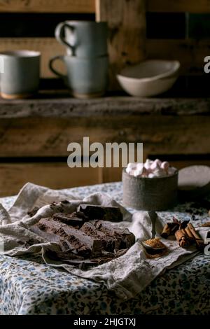 Ingredienti per preparare una bevanda calda invernale al cioccolato. Cioccolato fondente tritato, specie, zucchero di canna, marshmallows su tovaglia di lino rustico in cannella di campagna Foto Stock