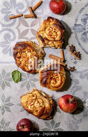 Dolci involtini di cannella appiccicosi alle mele da giardinaggio e bastoncini di cannella su sfondo ornato di piastrelle in ceramica. Panetteria tradizionale Foto Stock