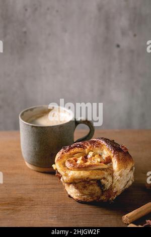 Dolce mela appiccicoso rotolo cannella pancia con tazza di caffè in piedi con bastoncini di cannella su tavola di legno. Panetteria tradizionale casa, spazio copia Foto Stock