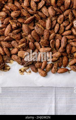 Miele glassato dolce e zucchero di canna mandorle tostate su carta di supporto su biancheria da cucina bianca. Spuntino dolce. Spazio di copia. Vista dall'alto Foto Stock