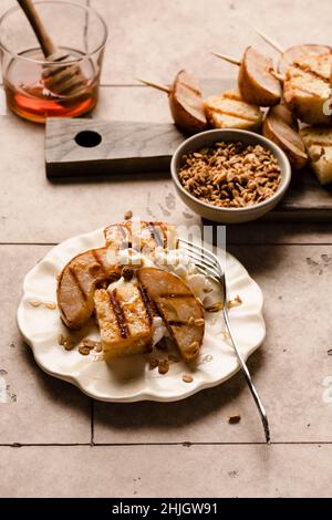 Torta alla sterlina e pere grigliate su un piatto con panna montata, miele e una spolverata di granola. Foto Stock