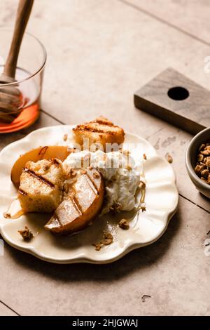 Torta alla sterlina e pere grigliate su un piatto con panna montata, miele e una spolverata di granola. Foto Stock