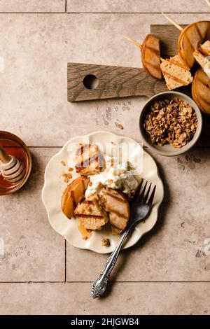 Torta di sterlina alla griglia e pere su un piatto con panna montata, miele, e una spruzzata di granola accanto a un bordo di servizio di spiedini cake di sterlina alla griglia e Foto Stock