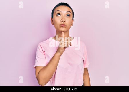 Bella donna ispanica con capelli corti indossando casual t shirt rosa pensiero concentrato sul dubbio con dito sul mento e guardando in su domandandosi Foto Stock