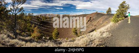 Un escursionista maschile che si erge sopra un piccolo cratere lungo il Tree Molds Trail. Craters of the Moon National Monument, Idaho Foto Stock