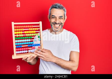 Bell'uomo di mezza età con capelli grigi che reggono abaco tradizionale aspetto positivo e felice in piedi e sorridendo con un sorriso sicuro mostrando denti Foto Stock