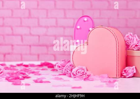 Composizione del giorno di San Valentino con rose rosa, petali di fiori, scatola regalo a forma di cuore di fronte a muro di mattoni con spazio copia Foto Stock