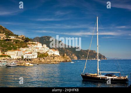 Barca a vela in mare contro la costa rocciosa e la città di Amalfi Foto Stock