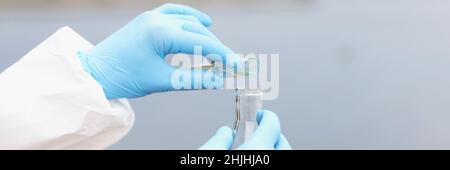 Lo scienziato in guanti e tuta protettiva versa l'acqua sporca dalla provetta al pallone Foto Stock