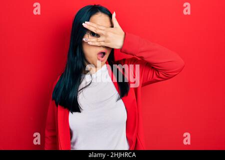 Bella donna ispanica con piercing naso indossando look casual e occhiali peeking in shock coprendo il viso e gli occhi con la mano, guardando attraverso le dita Foto Stock