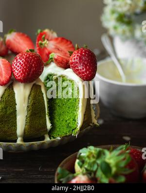 Torta di spinaci verdi con fragola su sfondo rustico scuro in legno. Ragazza in abito bianco che si glassa sulla torta. Primavera ancora vita Foto Stock