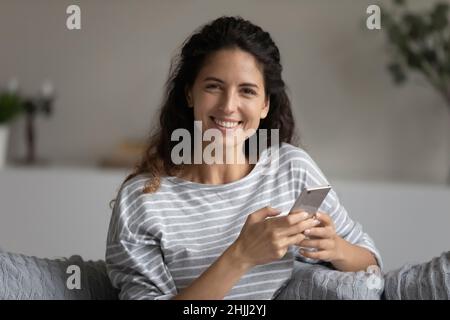 Giovane bella ispanica donna tiene il cellulare sorridente guardando la macchina fotografica Foto Stock