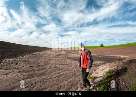 Un agronomo maschile esamina i campi dopo forti piogge sullo sfondo delle nuvole piovose. Valutazione dei danni meteorologici terreni agricoli dopo l'alluvione Foto Stock