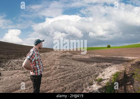Un agronomo maschile esamina i campi dopo forti piogge sullo sfondo delle nuvole piovose. Valutazione dei danni meteorologici terreni agricoli dopo l'alluvione Foto Stock