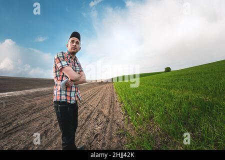 Un agronomo maschile esamina le colture di grano in un campo agricolo. Un coltivatore in un campo di grano fa note in un taccuino. Valutazione della resa del raccolto di grano Foto Stock