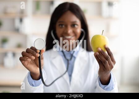 Nutrizionista afroamericano mostrante mela verde organica e usando stetoscopio, closeup Foto Stock
