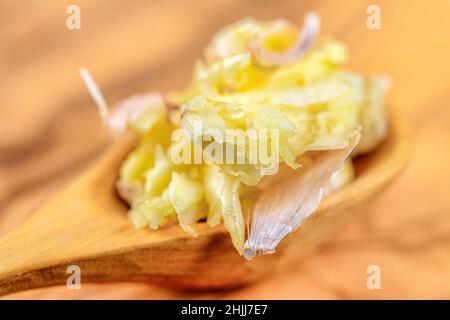 Primo piano morbido fuoco di cucchiaio di legname pieno di aglio pressato aromatico posto sul tavolo in cucina a casa Foto Stock