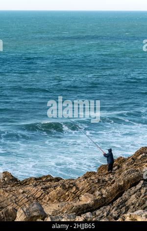 Persona che pesca sulla riva del mare Foto Stock