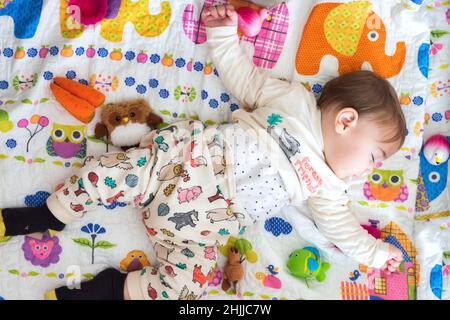 Adorabile bambino che dorme su un materasso colorato circondato da giocattoli Foto Stock