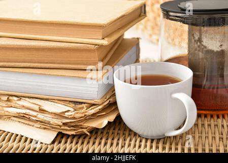 Pila di libri con tazza e teiera sul vassoio di vimini, primo piano Foto Stock