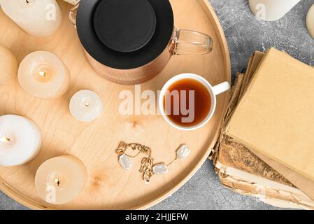 Vassoio con teiera, tazza, candele e libro su sfondo grunge Foto Stock