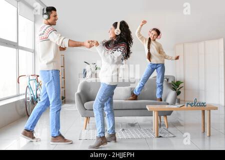 I genitori felici con la bambina in maglioni caldi e cuffie che ballano a casa Foto Stock