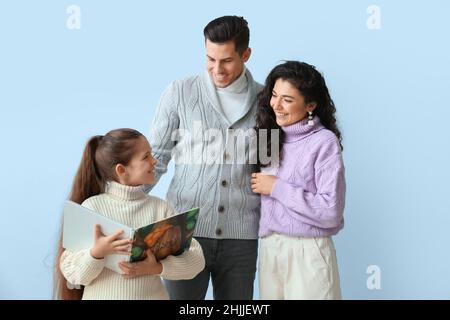 Bambina con i suoi genitori in maglioni caldi leggere libro su sfondo chiaro Foto Stock