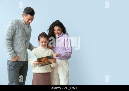 Bambina con i suoi genitori in maglioni caldi leggere libro su sfondo chiaro Foto Stock