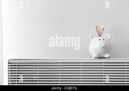 Piggy banca con banconote in euro sul radiatore. Concetto di stagione di riscaldamento Foto Stock