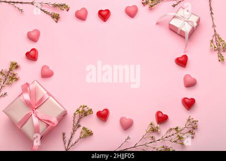 Cornice fatta di gustose caramelle a forma di cuore e fiori per la festa di San Valentino su sfondo rosa Foto Stock