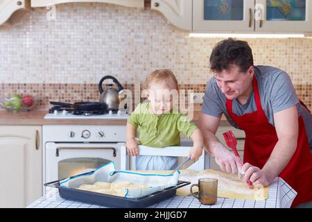 Papà insegna al bambino piccolo a preparare insieme biscotti o dolci da forno. Divertimento in famiglia a casa in cucina. Spazio di copia. Foto Stock