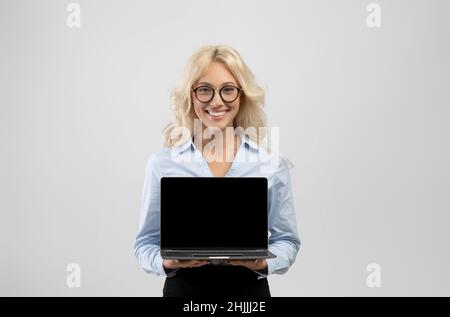 Felice giovane donna d'affari che tiene computer portatile con schermo vuoto per il tuo annuncio o sito web design Foto Stock