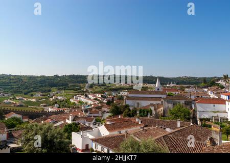 Vista panoramica di case bianche tetti di tegole rosse, e il castello dalla parete della fortezza. Bella città vecchia con medievale. Obidos villaggio, Portogallo. Estate domenica Foto Stock