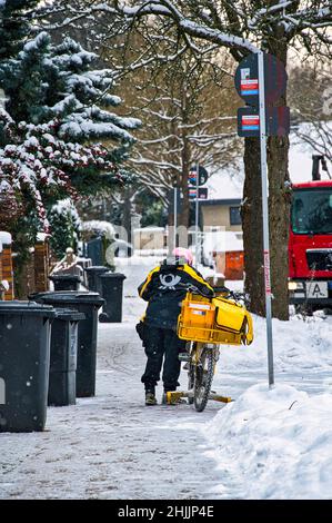 Berlino, Germania - 10th febbraio 2021: Un marciapiede nevoso con una mailwoman che spinge la sua moto. Foto Stock