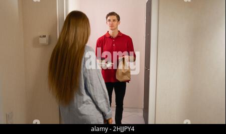 Consegna di cibo a casa, ristorante corriere dà il pacchetto al cliente alla porta, cena ordine e consegna, caucasico deliveryman e acquirente femminile a casa Foto Stock