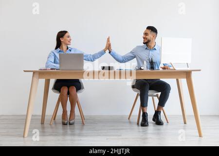 Ritratto di colleghi sorridenti che danno High Five seduti alla scrivania Foto Stock