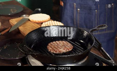 Frittura di hamburger su una griglia in ghisa. Riprese in stock. La pattina di hamburger viene preparata sulla teglia. Foto Stock