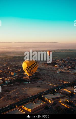 Meraviglioso colpo verticale di due palloncini che volano a bassa altitudine sopra le case di luxor egitto. Paesaggi dell'egitto in lontananza, mattina presto Foto Stock