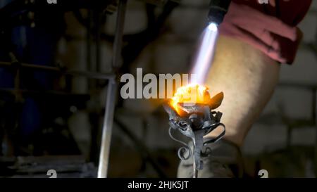 Il fabbro allinea le foglie di ferro rosa e fa la forma finale del fiore. Il fabbro fa rosa di ferro. Foto Stock