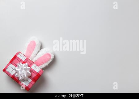 Morbide orecchie di un coniglietto pasquale con una scatola regalo su sfondo grigio. Spazio di copia, vista dall'alto, disposizione piatta. Foto Stock