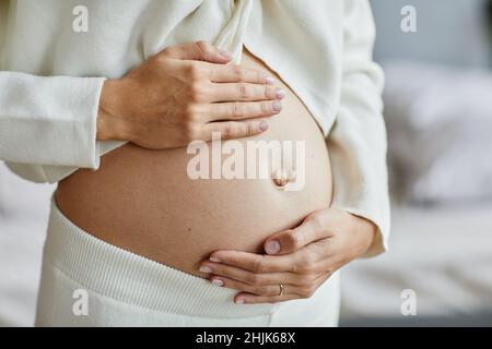 Primo piano di una giovane donna incinta che tocca il ventre e si prende cura della sua salute Foto Stock
