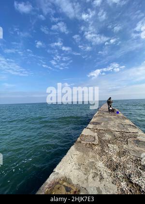 Scatto verticale di un pescatore sul molo di mare in una giornata di sole Foto Stock